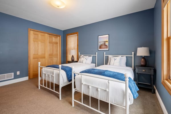 A cozy bedroom with two white iron beds, blue decorations, and warm wooden accents.