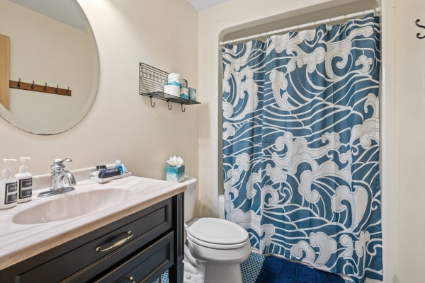 A small bathroom with a circular mirror, a wave-patterned shower curtain, and blue accents.