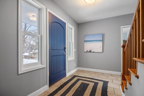A welcoming entryway with a navy blue door, light gray walls, and beach-themed artwork.