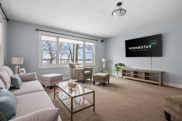 A bright living room featuring a sofa, armchair, and large windows overlooking nature.