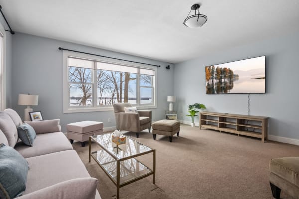 A cozy living room featuring a sectional couch, coffee table, and large windows with a view of trees and water.