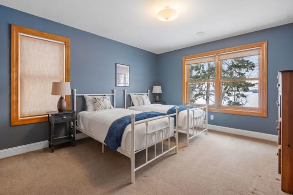 A cozy bedroom with two twin beds, soft lighting, and a view of trees outside.
