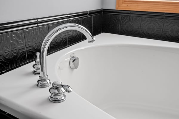 Close-up of a modern bathtub with chrome fixtures and black tiled walls.