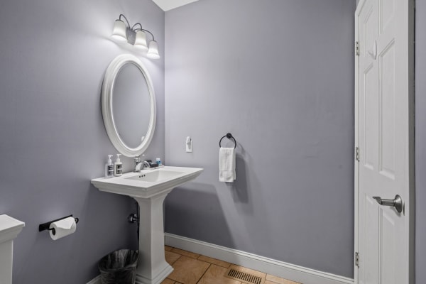 Minimalistic bathroom with a lavender wall, white pedestal sink, and round mirror with fixtures.