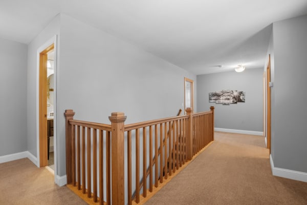 Upstairs hallway with a wooden banister and gray walls, leading to doors and artwork.