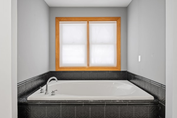 A spacious bathroom with a white bathtub and gray walls, illuminated by natural light from two windows.