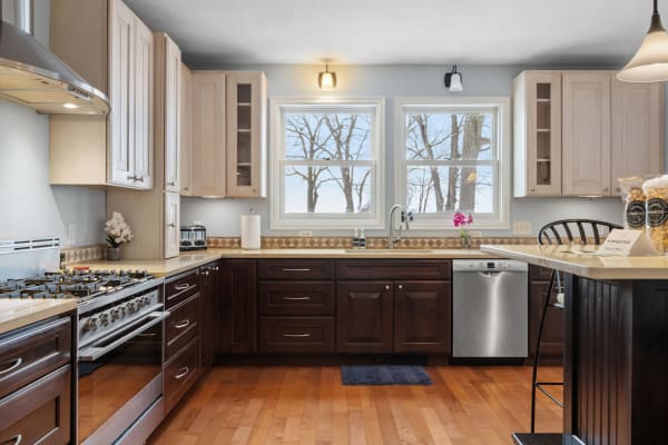 Modern kitchen with light and dark cabinetry, large windows, and wooden flooring.