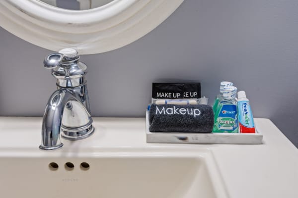 Bathroom sink with a chrome faucet, gray hand towel labeled 'Makeup', and toiletries organized in a tray.