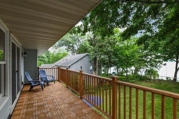 A wooden balcony with blue chairs overlooking a grassy area and trees.