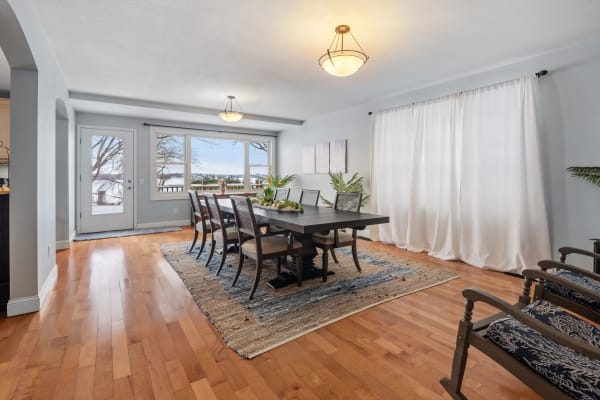 Dining room with wooden table, chairs, and large windows overlooking nature.