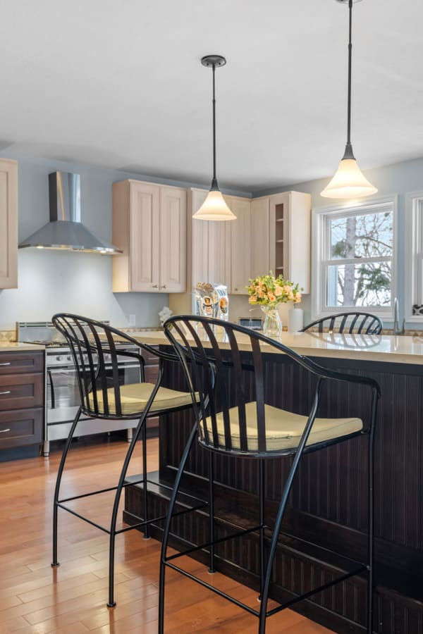 Interior view of a modern kitchen with an island and bar stools, set with fresh flowers and pendant lighting.
