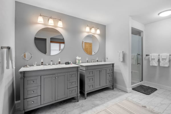 Modern bathroom featuring gray vanities, large mirrors, and a glass shower enclosure.