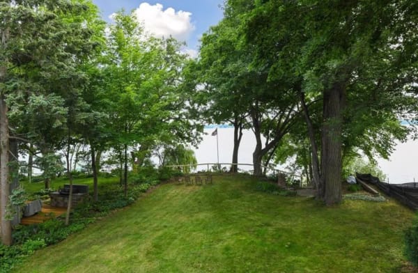 A beautifully landscaped yard with chairs overlooking a calm lake, framed by trees and blue skies.