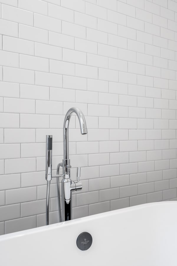 Close-up of a white bathtub with a chrome faucet and subway tiled wall.