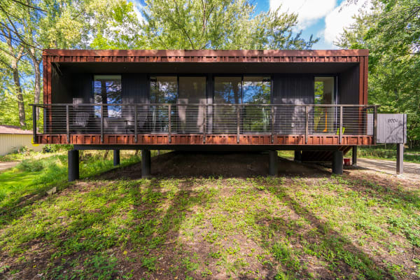 A sleek, modern home with glass windows and a balcony, elevated amidst greenery.