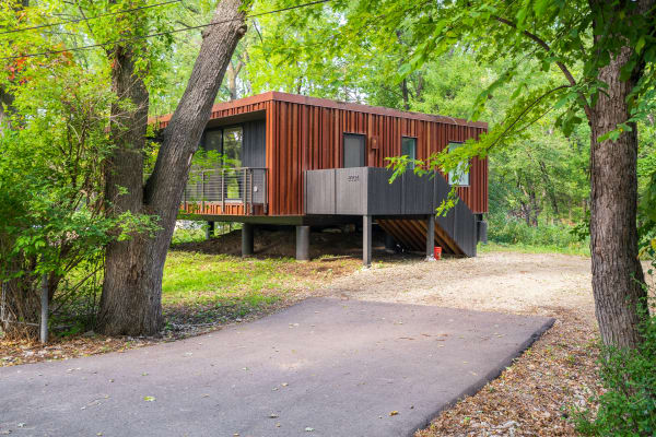 Modern house elevated on stilts, surrounded by trees and greenery.