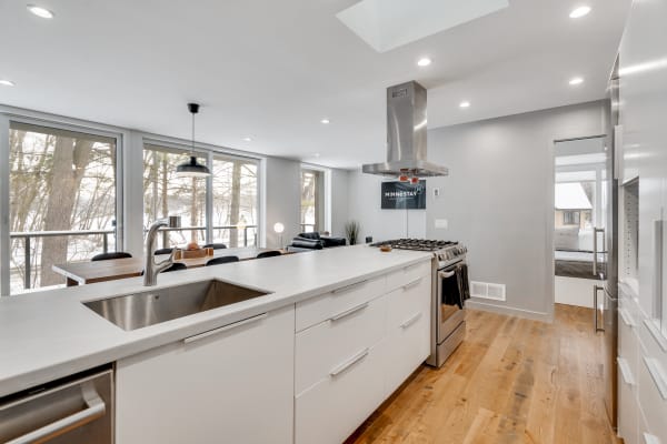 Sleek modern kitchen with a white island and large windows overlooking trees.