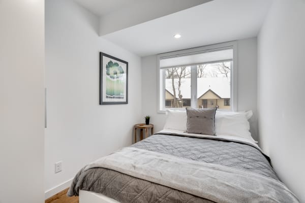 A minimalist bedroom featuring a bed with a gray blanket, a side table, and a view of snow outside.