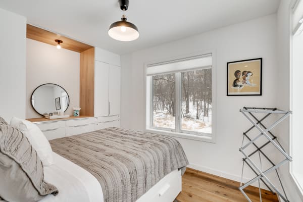 A cozy modern bedroom featuring a gray quilt and white cabinetry with a large window overlooking a snowy scene.