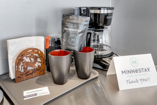 A coffee station with black and red mugs, a coffee maker, coffee package, and a thank you note from MINNESTAY.