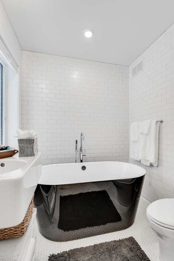 A contemporary bathroom with a black freestanding bathtub, white subway tiles, and hexagon flooring.