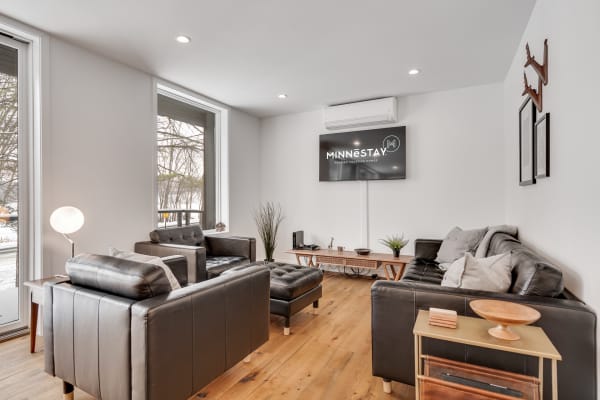 Contemporary living room featuring black leather sofas, a TV, and natural light from large windows.