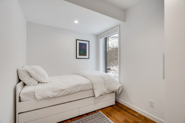 Minimalistic bedroom with a single bed and a view of snow outside.