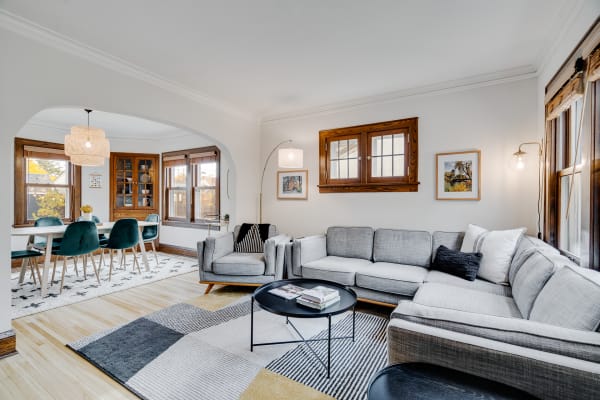 Stylish living room with gray sectional sofa, black coffee table, and a dining area with green chairs in the background.