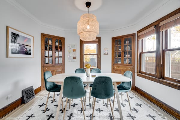 A modern dining room with an oval table, velvet chairs, and two wooden cabinets. A woven pendant light hangs above the table.