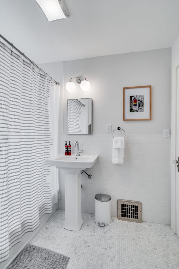 Contemporary bathroom featuring a pedestal sink, striped shower curtain, and marble flooring.
