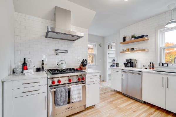 Modern kitchen with white cabinets, stainless steel appliances, and wooden shelves.