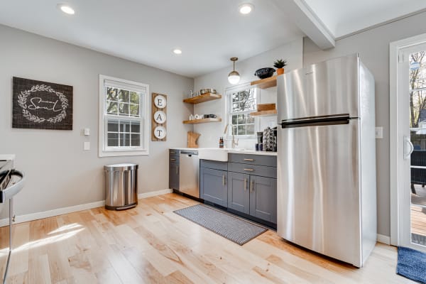 A modern kitchen with a stainless steel refrigerator, dark gray cabinets, and wooden shelves filled with kitchen items.