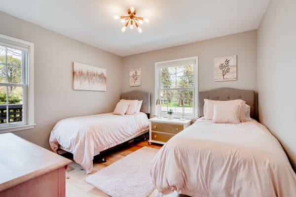 A twin bedroom featuring two beds, pastel decor, and natural light through a window.