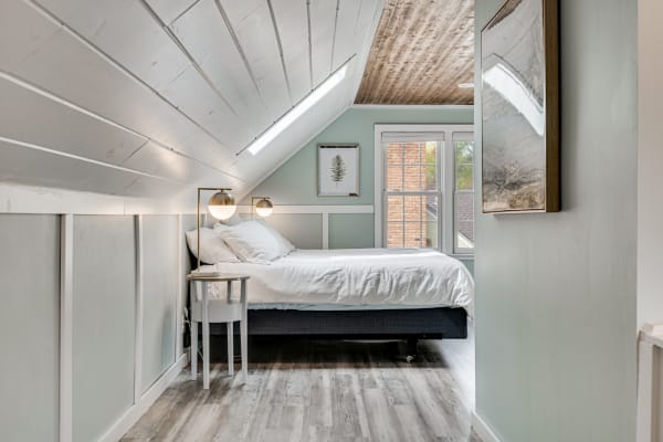 A cozy attic bedroom featuring a slanted ceiling, white bed linens, and large windows.