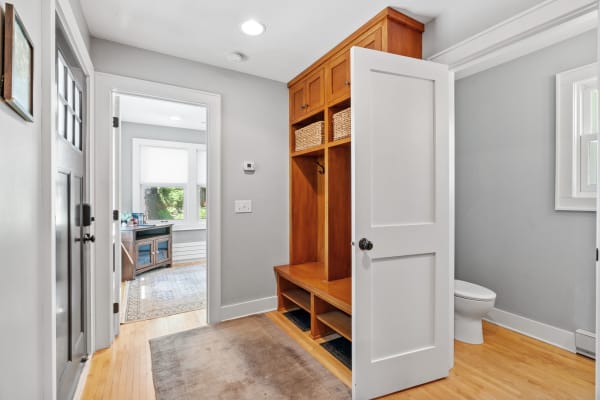 A bright entryway featuring a coat closet, built-in bench, and windows leading into another room.