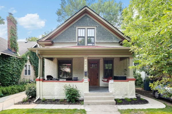 A charming bungalow with green shingles and beige exterior, featuring a front porch with a swing.