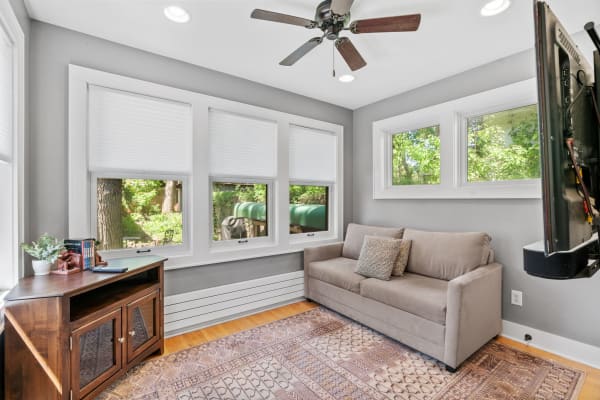 Interior view of a sunroom with a gray wall, sofa, and large windows revealing greenery outside.