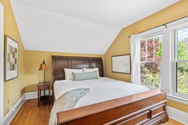 A cozy bedroom featuring a wooden bed, warm yellow walls, and natural light from the window.