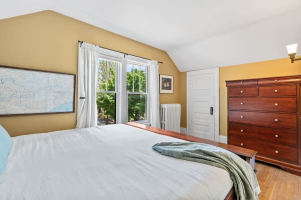 Cozy bedroom featuring a bed, wooden dresser, and large windows.