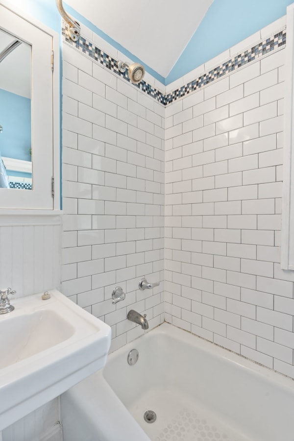 A bathroom with white subway tiles, a small sink, and a bathtub.