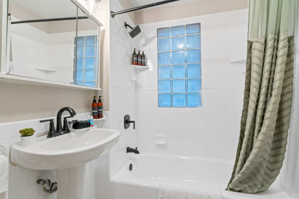 A clean and modern bathroom featuring a white pedestal sink, bathtub, and a green shower curtain.