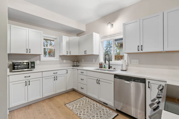 Modern kitchen featuring white cabinets, wood flooring, and a stylish black faucet.