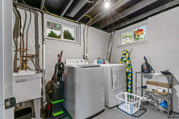 A compact laundry room with a washing machine, dryer, ironing board, and various supplies on shelves.