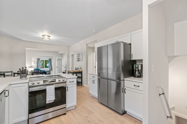 Modern kitchen with stainless steel fridge, white cabinets, and wooden flooring.