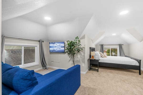 Cozy attic room featuring a blue couch, bed, indoor plant, and mounted television.