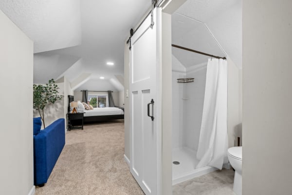 Interior view of a bedroom with an attached modern bathroom, showing a sliding barn door and cozy furnishings.