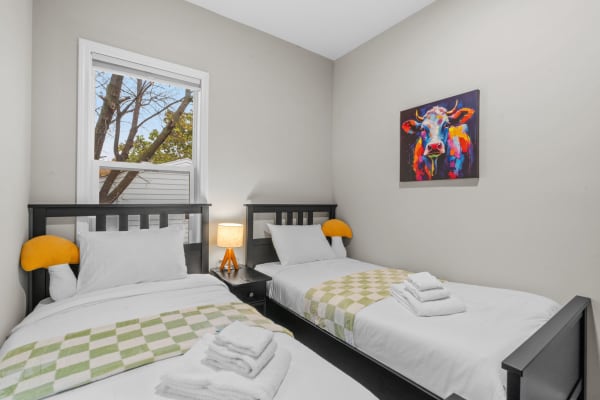 A cozy room with two single beds, a colorful cow painting, and a view of trees outside.