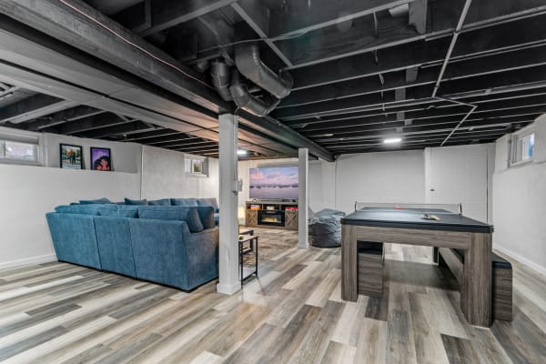 A well-decorated basement featuring a blue sectional sofa, a gaming table, and a large TV.