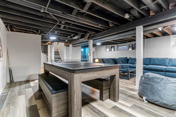 Interior view of a modern basement featuring a ping pong table and a blue sectional sofa.