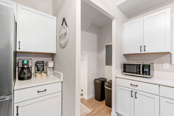 A contemporary kitchen with white cabinets, a coffee station, and black trash bins.